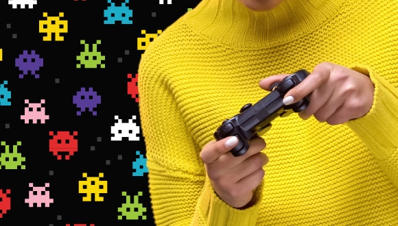 a person in a yellow sweater holding a game console against a "Space Invaders" style background